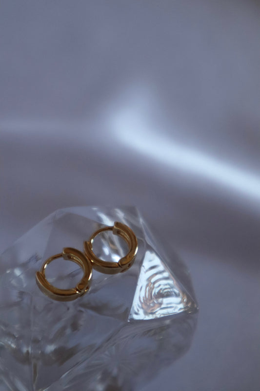Close-up of 18K gold plated 11mm huggies earrings displayed on prop by Nayda De Jesus