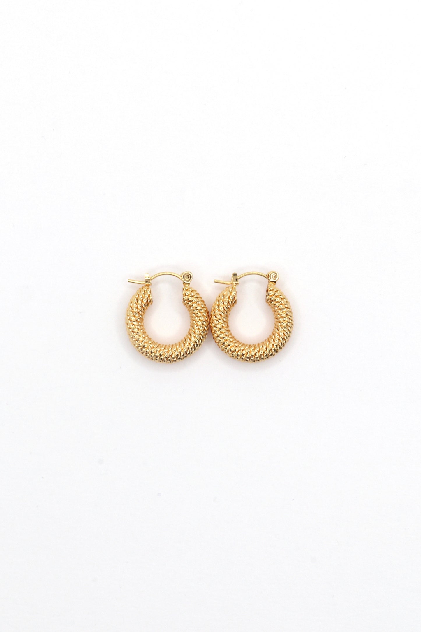 Close-up of 18K gold plated 20mm twisted hoop earrings on white background by Nayda De Jesus