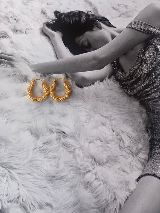 Close-up of 18K gold plated 20mm twisted hoop earrings displayed on magazine by Nayda De Jesus