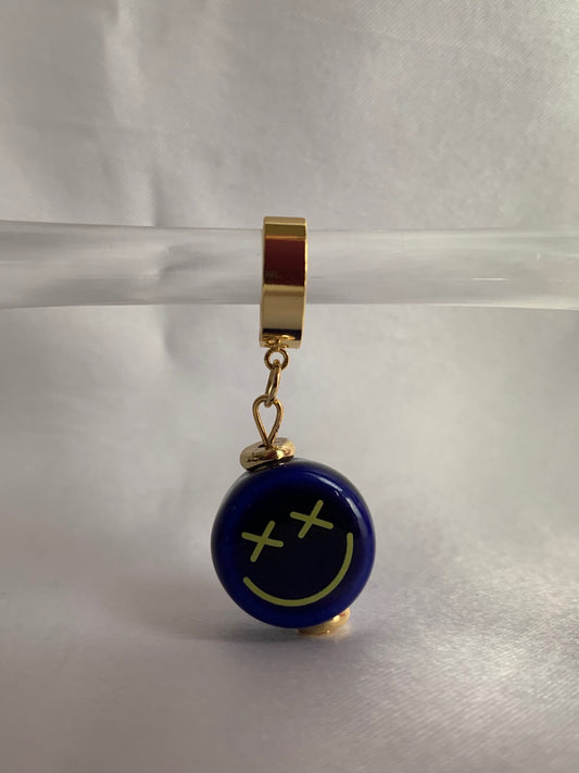 18K gold plated huggie hoops with blue ceramic smiley face charm displayed on prop