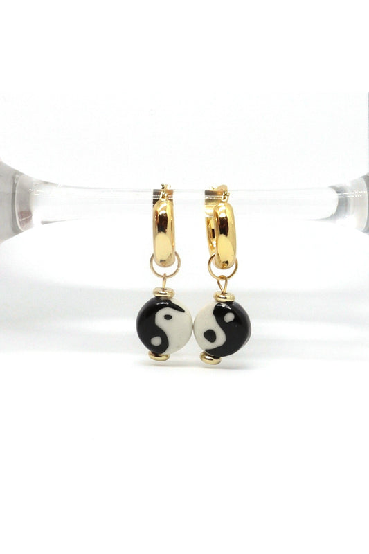 Ceramic Yin Yang earrings with 18K gold plated hoops displayed on prop with white background by Nayda De Jesus