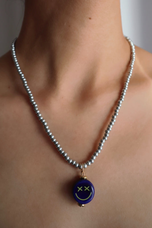 Stylish metallic glass necklace with blue crossed eyes smiley face ceramic pendant charm worn on model's neck
