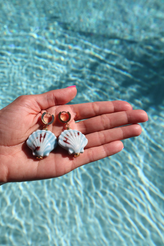 Close-up of gold huggie earrings featuring ocean-blue sea shell pendants