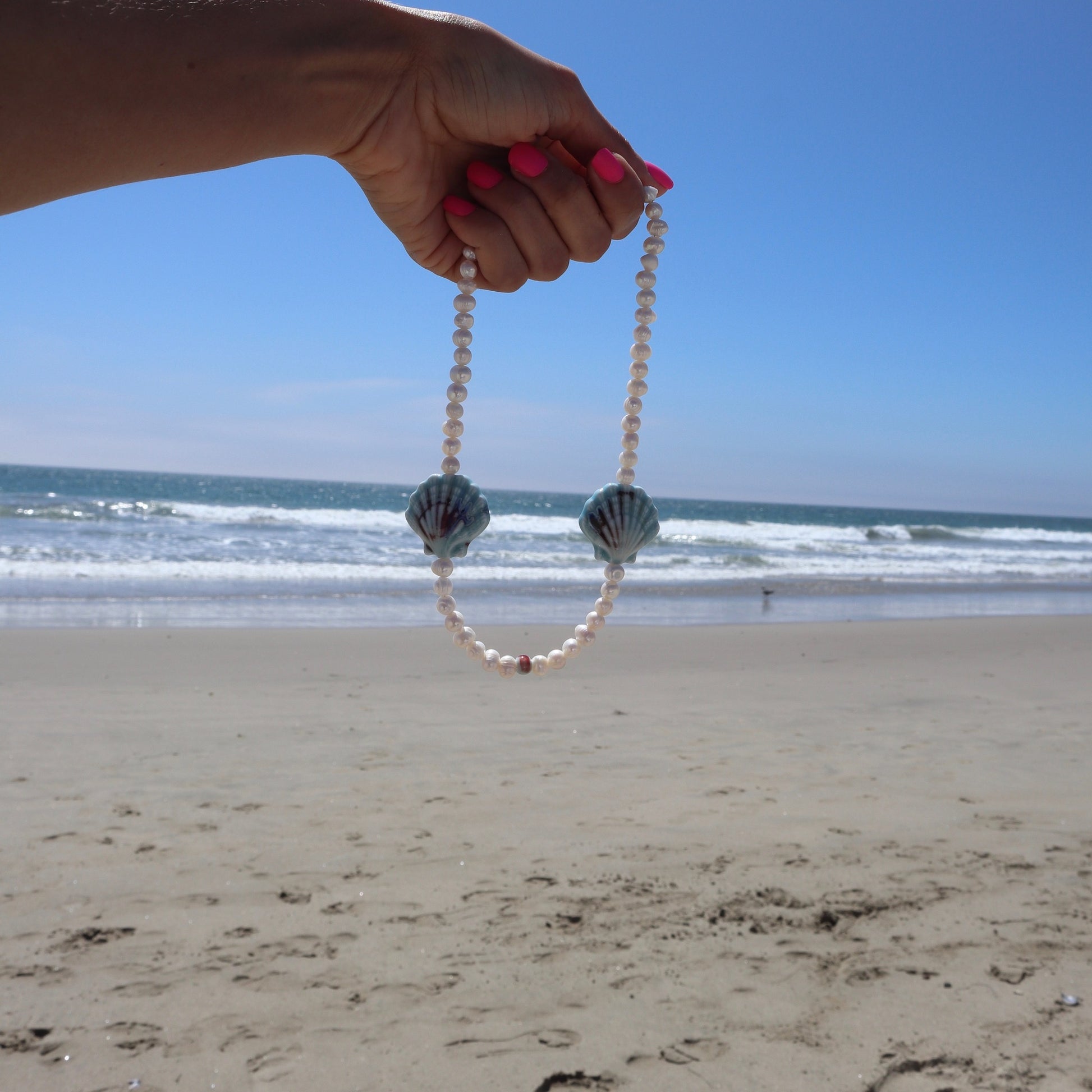 lifestyle-photo-at-the-beach-of-cordelia-necklace-blue-ceramic-sea-shells-freshwater-pearls-18-k-gold-filled-spring-clasp-by-nayda-de-jesus