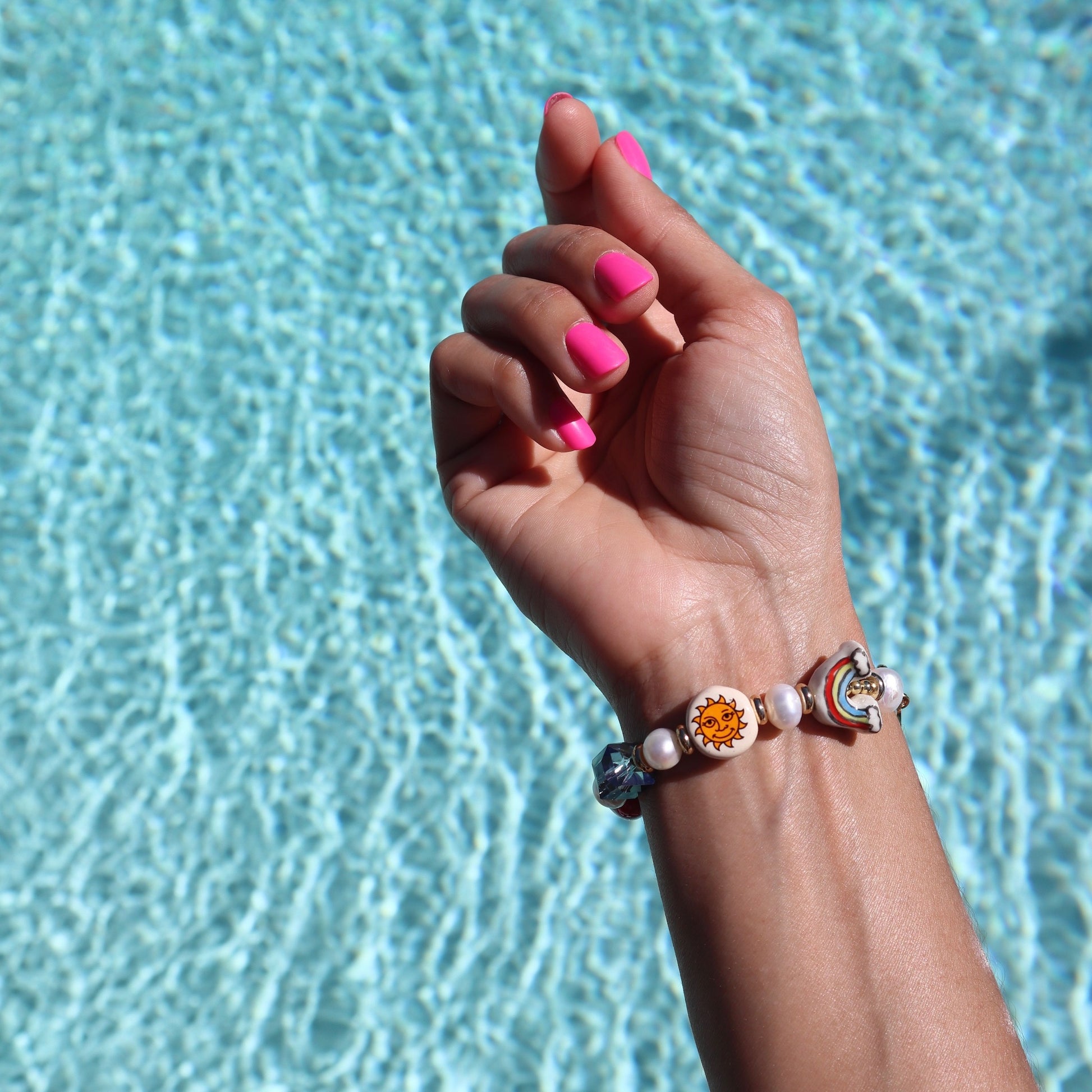 lifestyle-photo-by-pool-of-karol-g-manana-sera-bonito-tropical-bracelet-freshwater-pearls-ceramic-heart-mermaid-sun-rainbow-beads-iridescent-blue-glass-stone-by-latina-artist-nayda-de-jesus