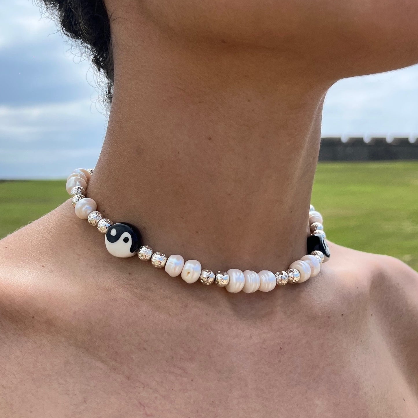 lifestyle-photo-at-el-morro-san-juan-puerto-rico-of-daniel-necklace-made-with-ceramic-yin-yang-fresh-water-pearls-metallic-lava-beads-along-18-k-spring-clasp-closure-by-nayda-de-jesus