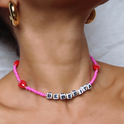 lifestyle-photo-of-bebesita-necklace-customizable-with-cube-letters-made-with-red-ceramic-hearts-and-pink-glass-beads-along-18-k-gold-filled-spring-clasp-by-nayda-de-jesus